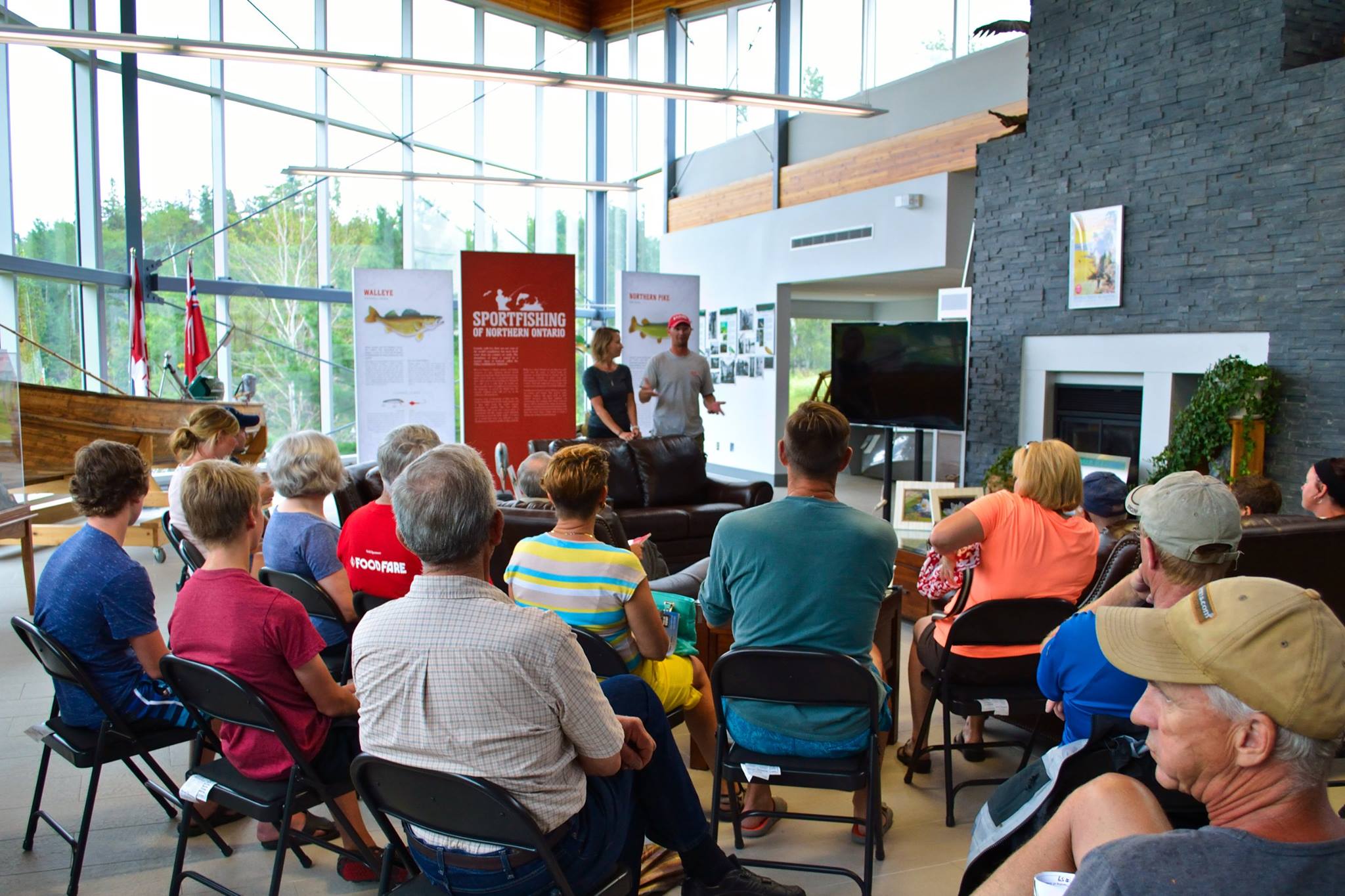 A group of people on folding chairs listen to two people give a talk on species of fish in Northern Ontario