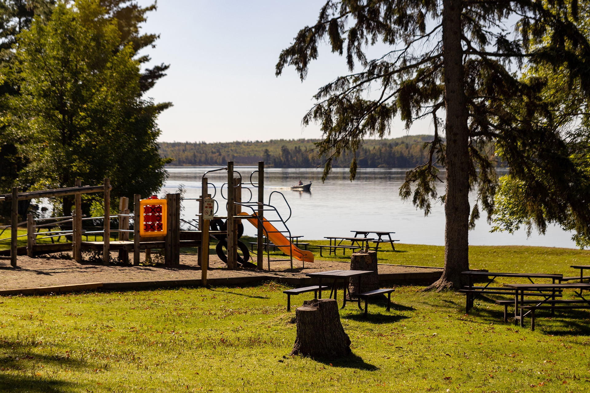 A large wooden play structure in a sandbox beside a lake