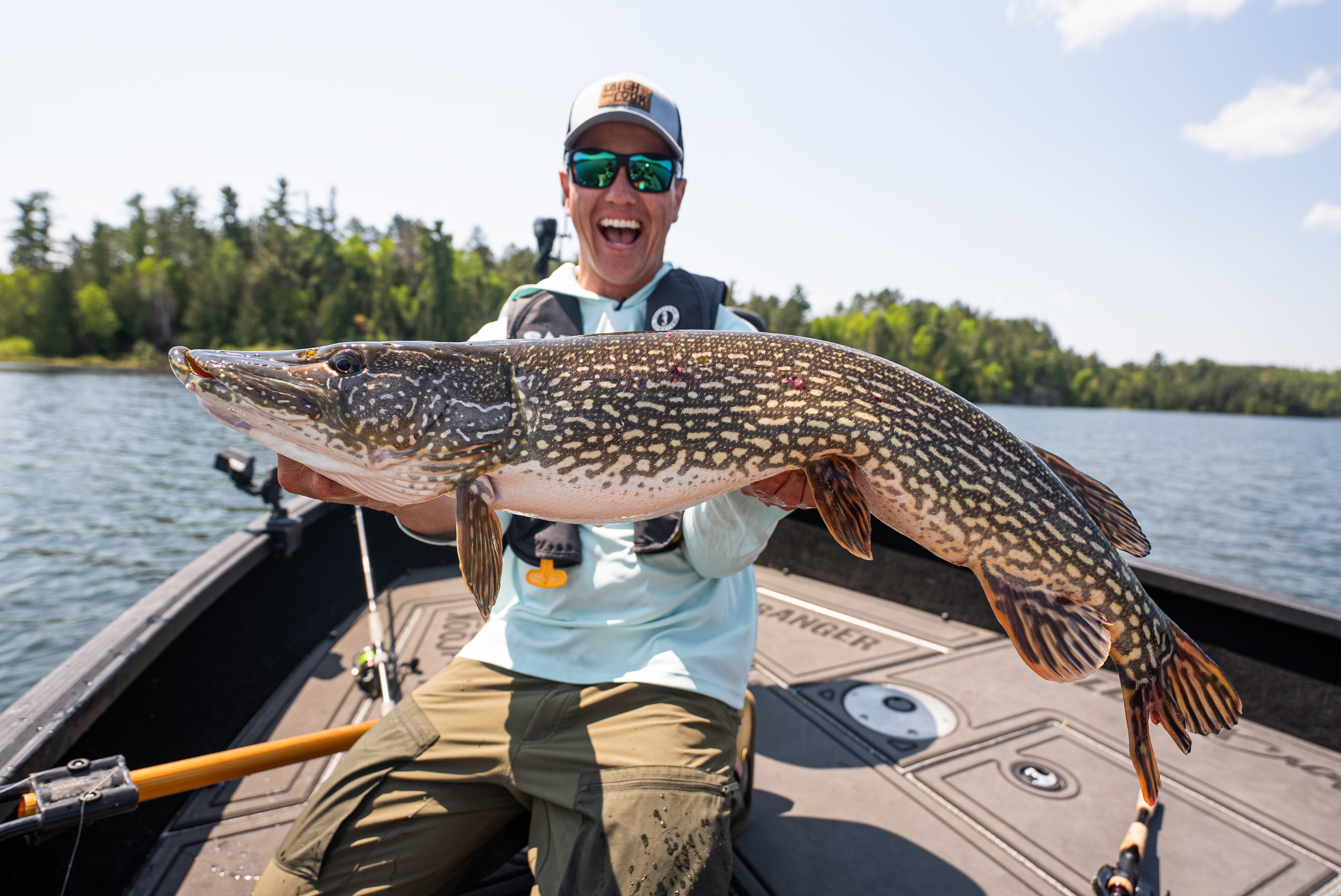 A man wearing sunglasses and a baseball cap holds up a large fish he's just caught