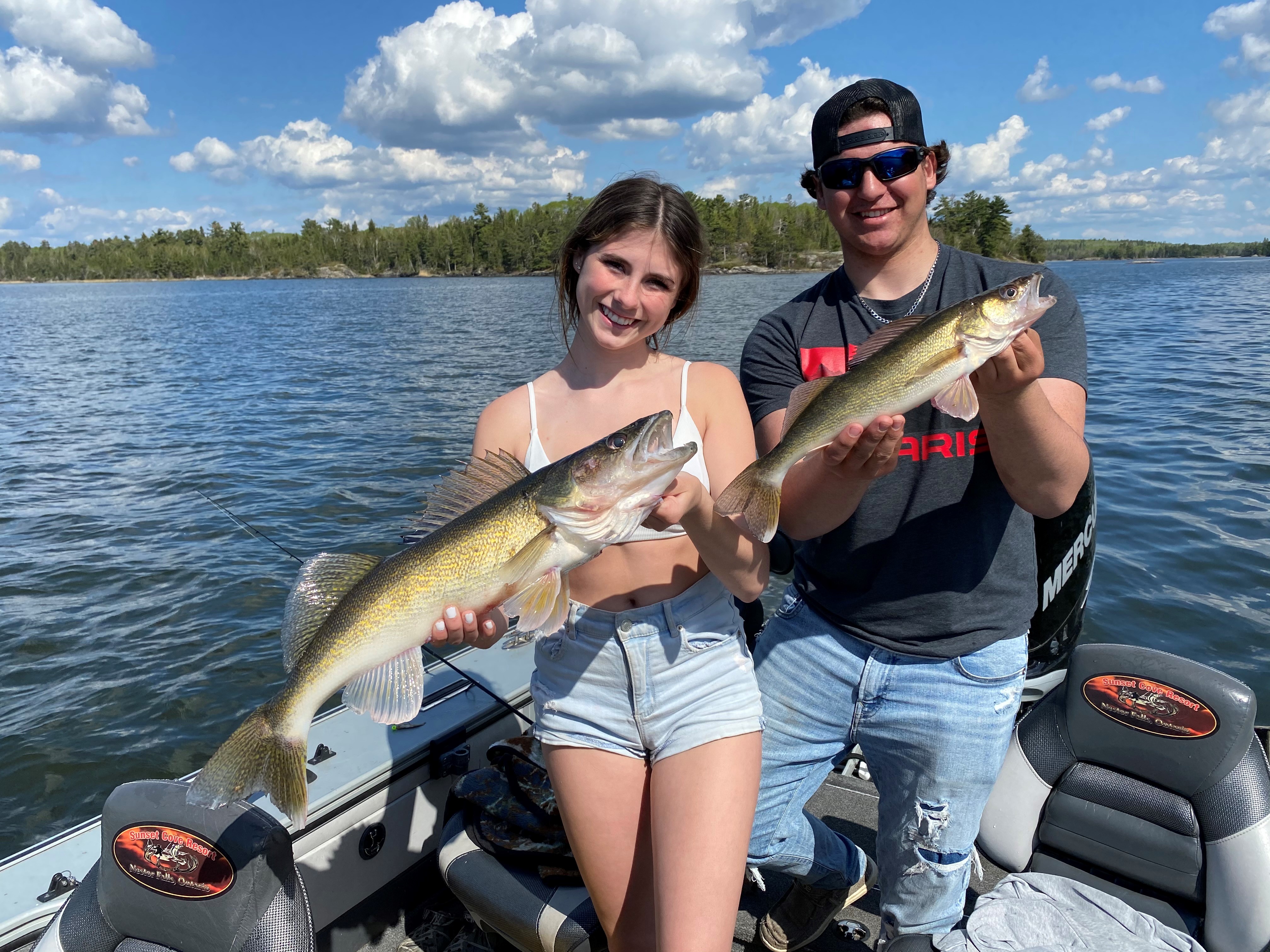 A young woman and a young man hold up two large fish they just caught