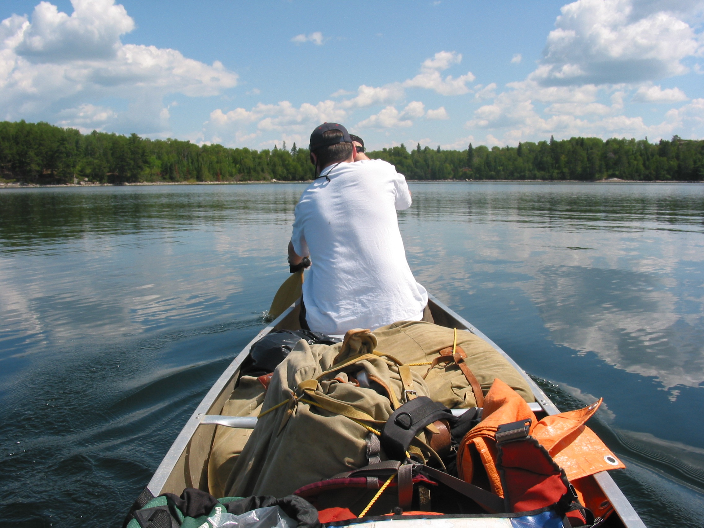 A person in a white shirt sits in the bow of a canoe and paddles