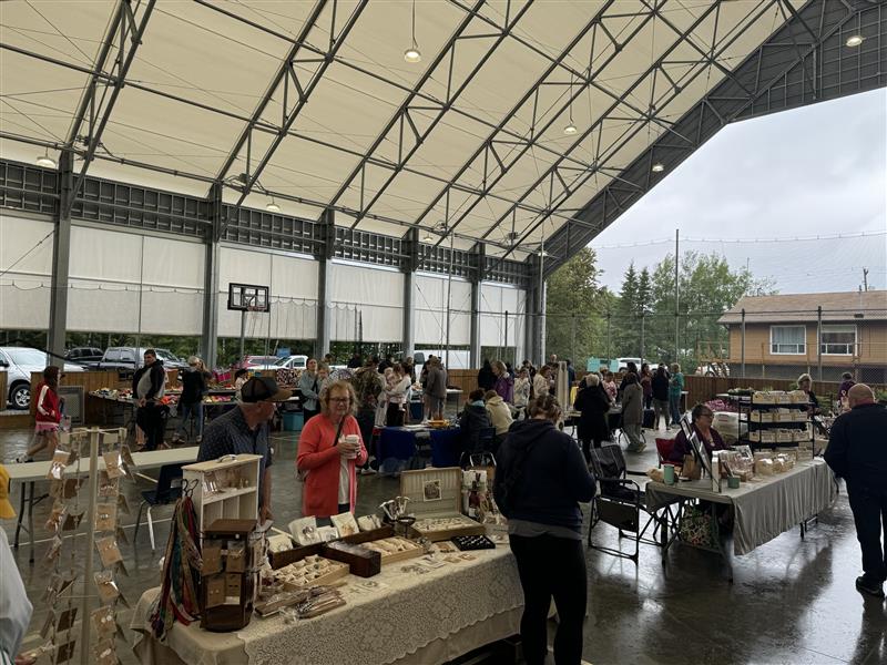 People shopping at various long tables of local goods at a covered recreation facility